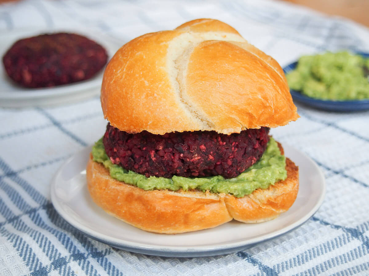 black bean beet burger on plate with additional burger and guacamole in background behind