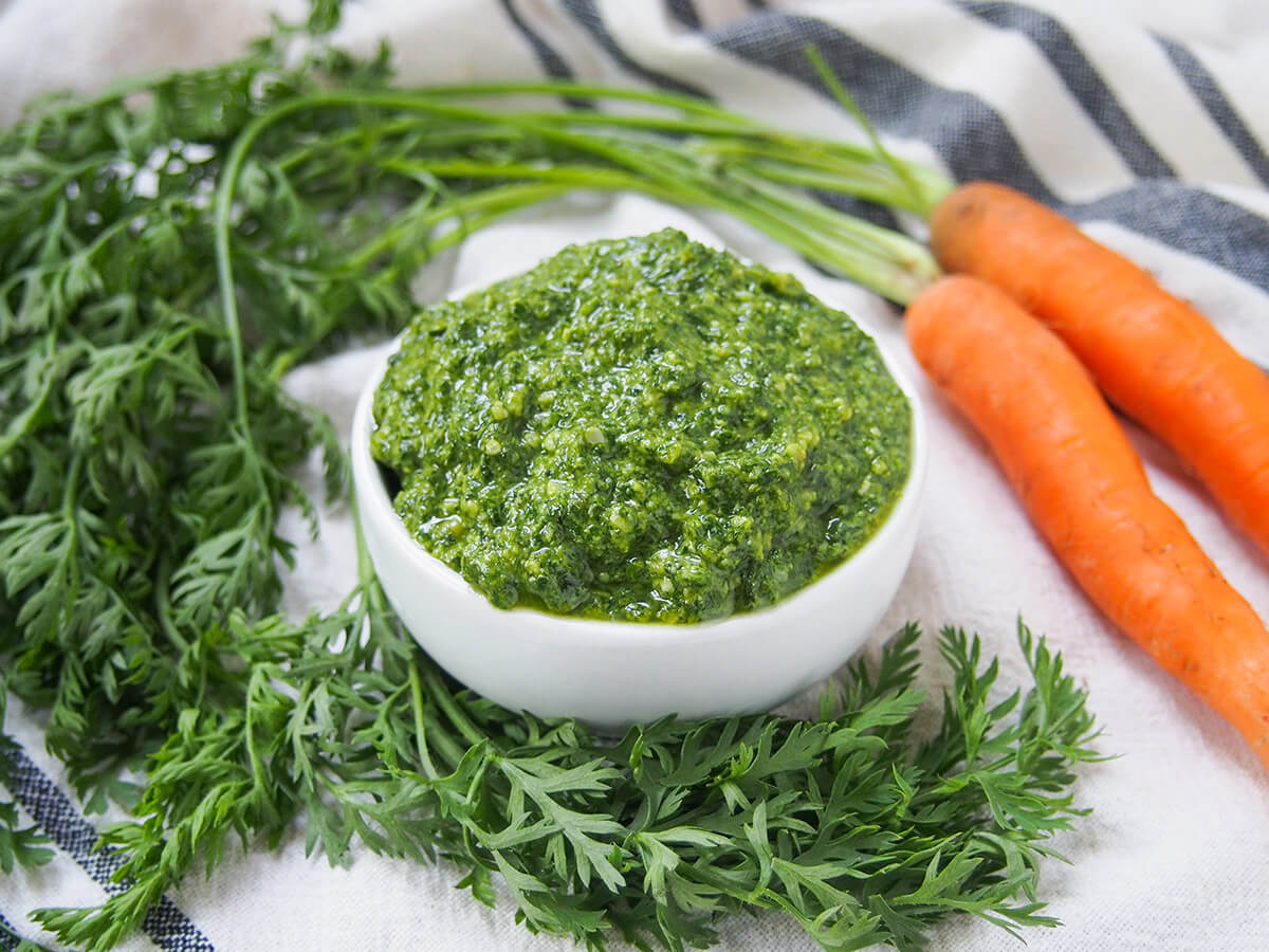 bowl of carrot top pesto with carrot greens and carrots around bowl