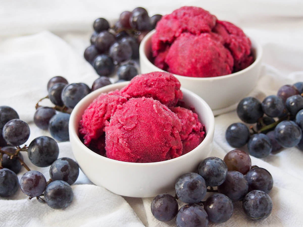 bowl of Concord grape sorbet with second bowl behind and grapes around bowls.