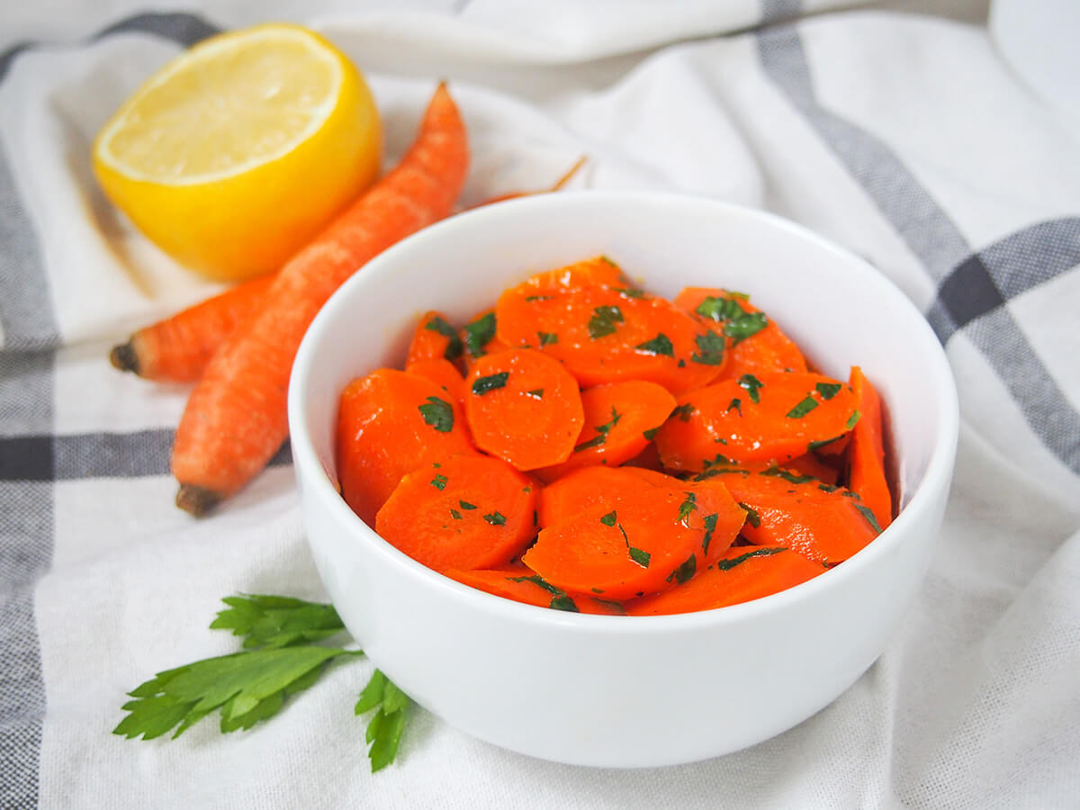 side view of bowl of vichy carrots on white cloth.