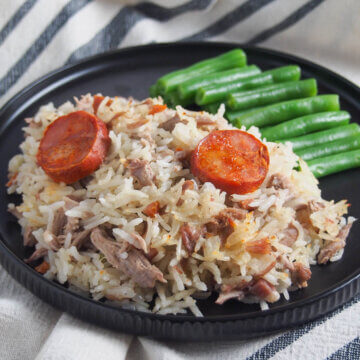plate of arroz de pato Portuguese duck rice with green beans behind.