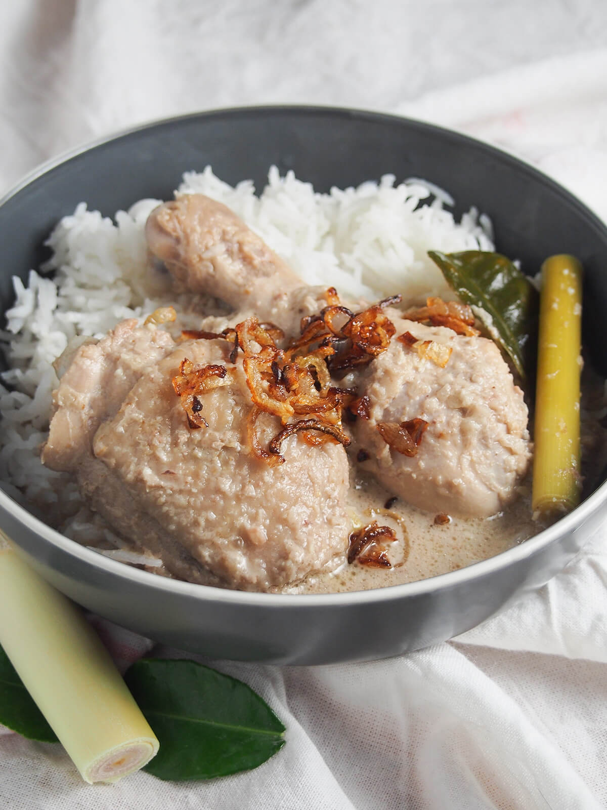 Opor ayam is an easy, aromatic coconut-based Indonesian chicken curry/stew with  flavors of ginger, garlic and lemongrass. Comforting and so tasty. side view of bowl of opor ayam Indonesian coconut chicken served with rice.