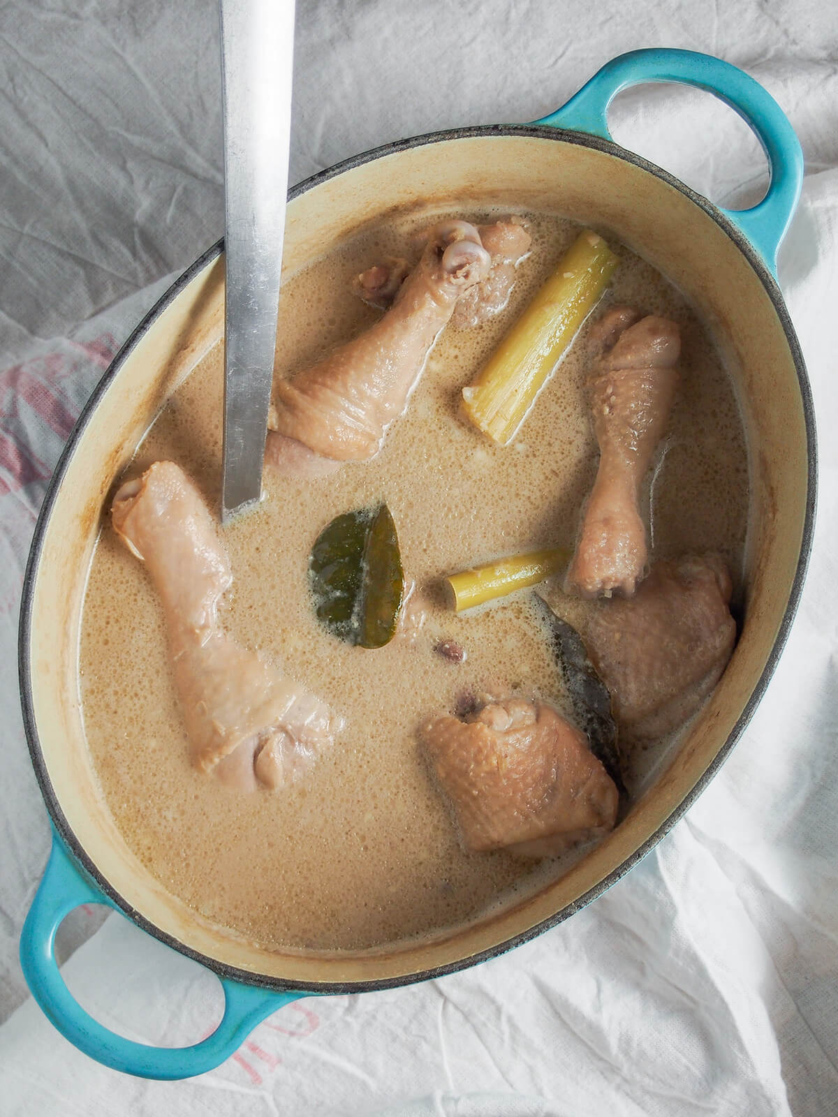 Opor ayam is an easy, aromatic coconut-based Indonesian chicken curry/stew with  flavors of ginger, garlic and lemongrass. Comforting and so tasty. pot of opor ayam Indonesian coconut chicken with lemongrass stems, lime leaves and chicken showing through sauce.