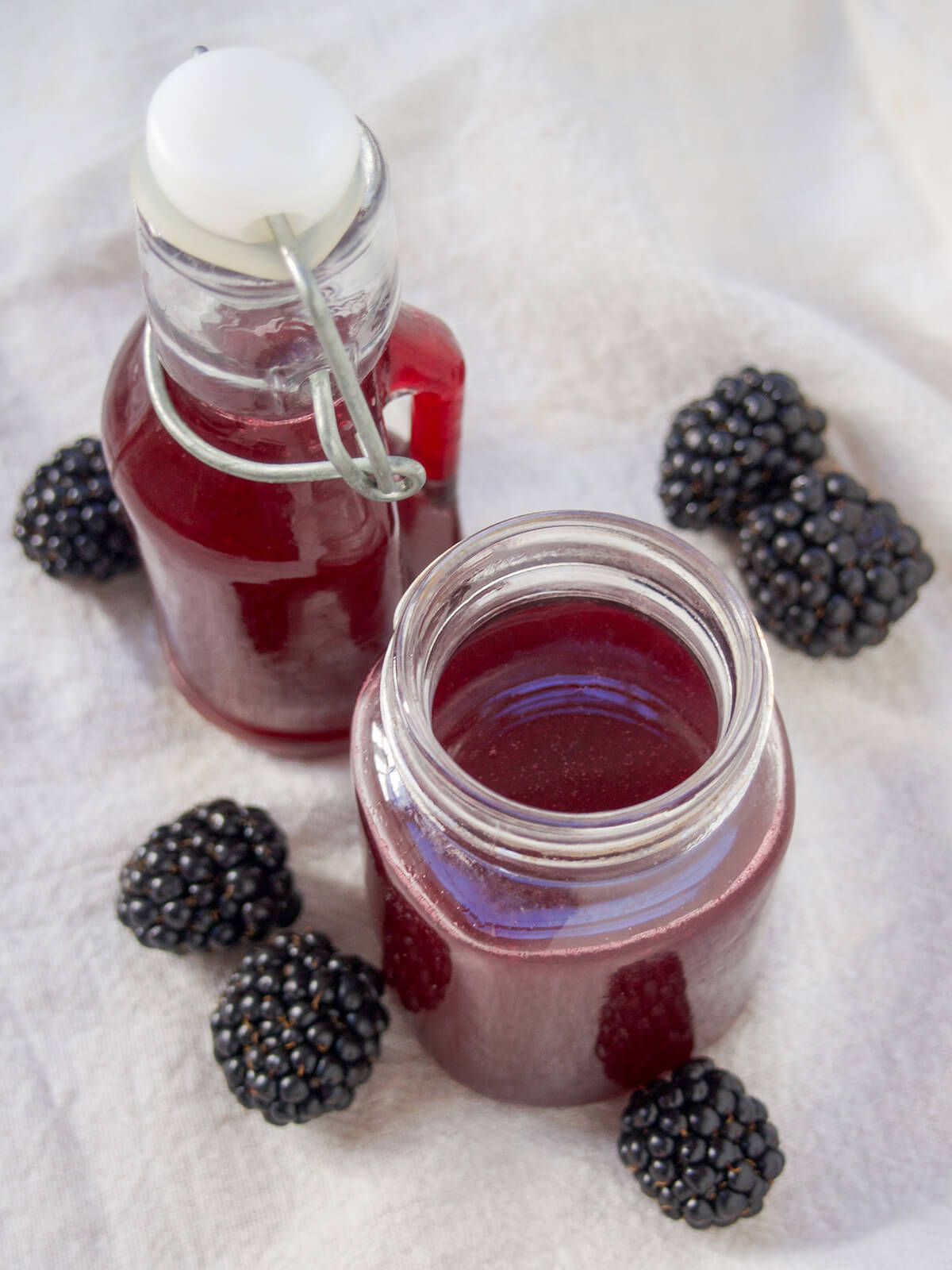 This blackberry simple syrup is an easy way to add some bright berry flavor and color to cocktails, lemonade or make a simple soda. It's quick to make, versatile, and great to enjoy all summer long. overhead view looking into jar of blackberry simple syrup with bottle behind it and blackberries around.