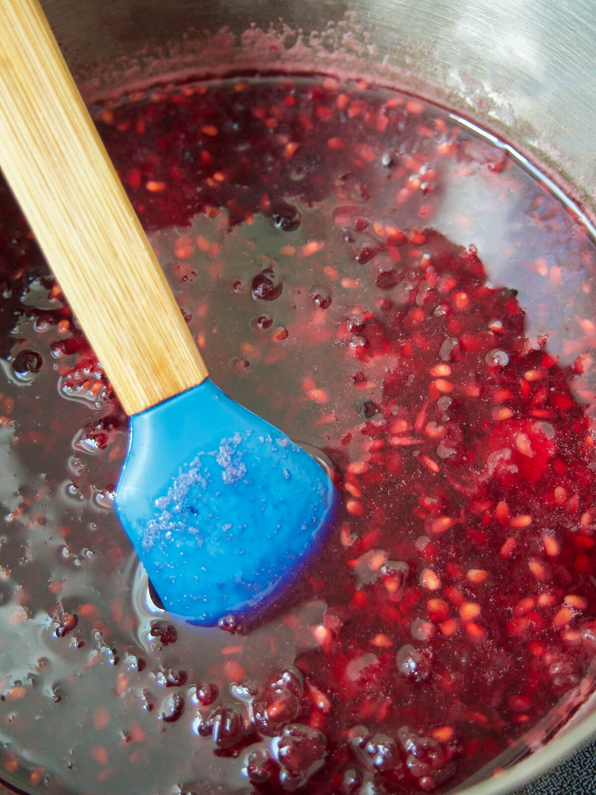blackberry syrup in pot before straining spatula in pan with mashed blackberries in liquid