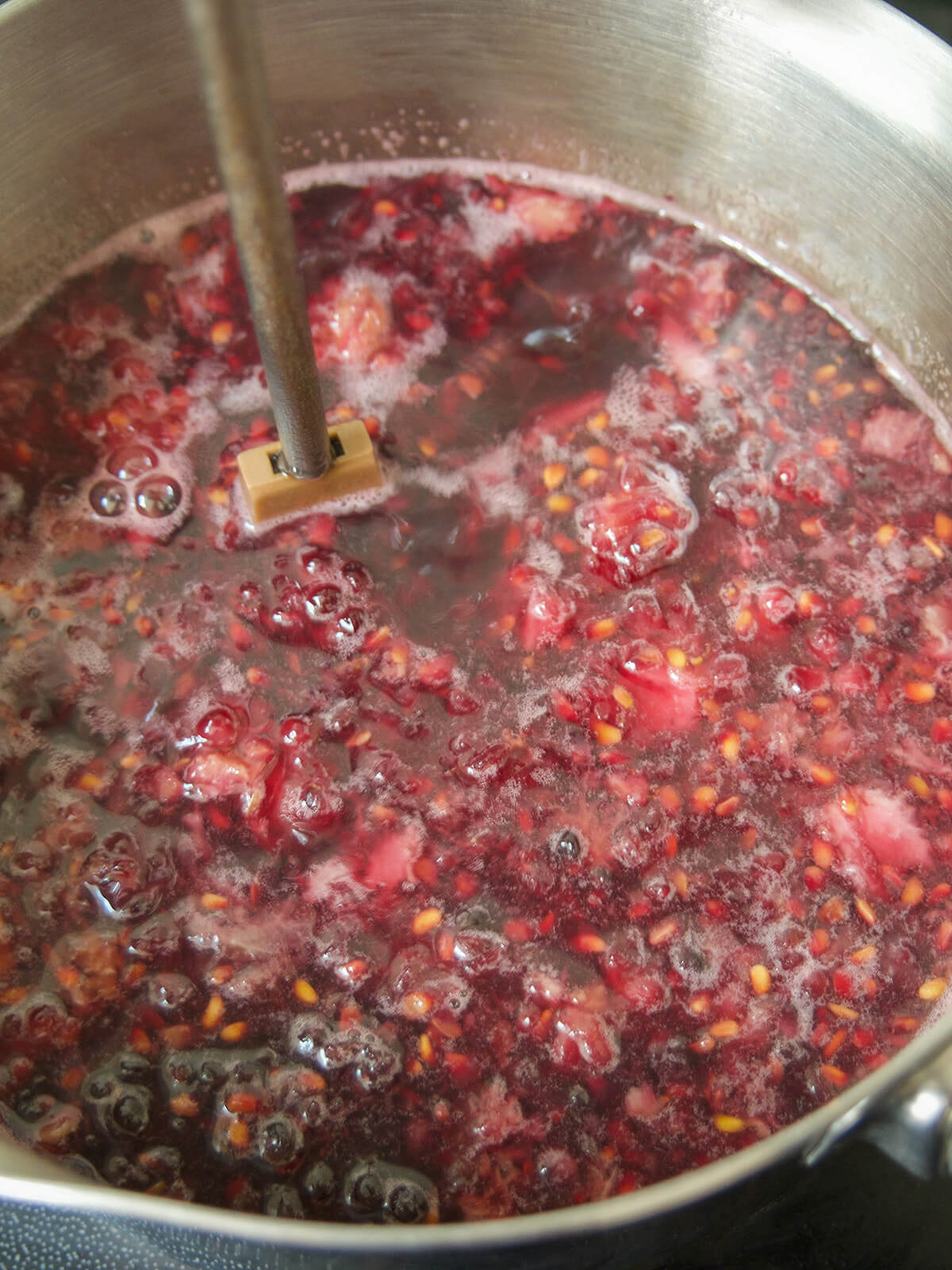 mashing blackberry simple syrup masher in simmering blackberry mixture in pot.