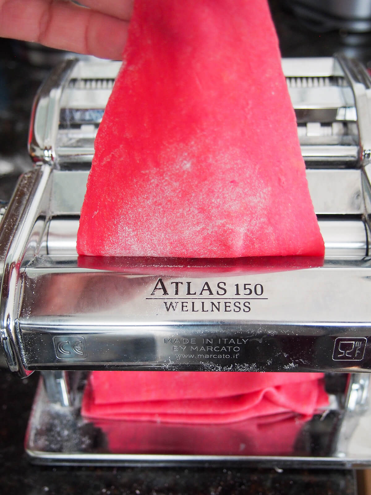 rolling beet pasta dough rolling a sheet of beet pasta dough through pasta machine.