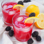 two glasses of blackberry lemonade garnished with blackberries and slice of lemon.