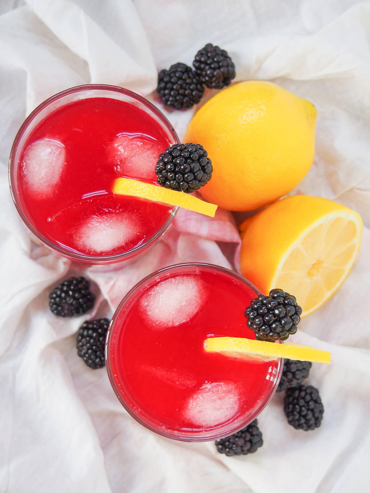 overhead view of two glasses of blackberry lemonade with lemons and blackberries to side of glasses.