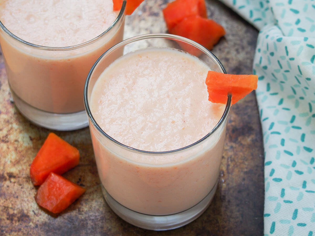 This papaya milkshake is creamy, fruity, cool and delicious. It's easy to make, refreshing and the delicate tropical flavor is perfect for a warm day (or to imagine you're somewhere warm). glass of papaya milkshake with pieces of papaya to side.