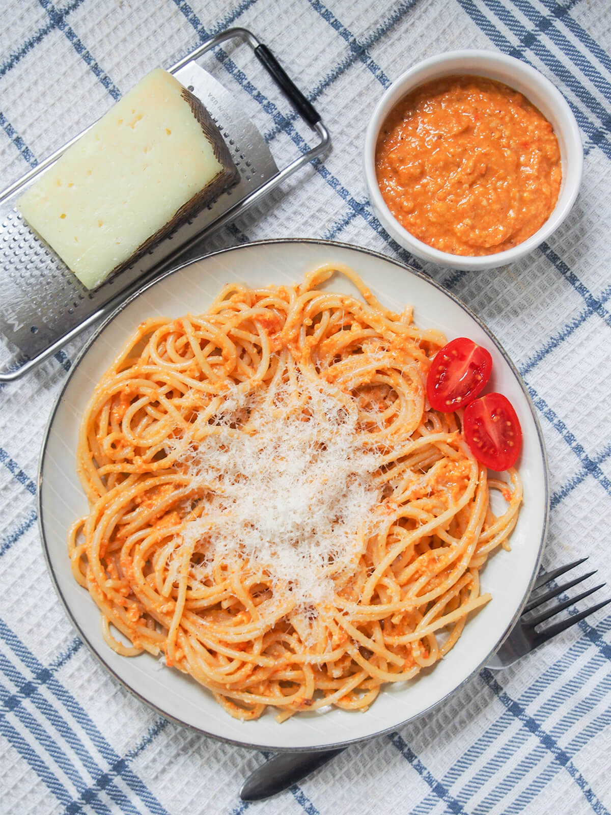 Romesco pasta is a super easy pasta dish that's perfect for any night. Spanish romesco sauce is packed with tasty flavor from tomato, nuts and more that wraps deliciously around the pasta. overhead view of plate of romesco pasta with cheese and dish of romesco sauce above.