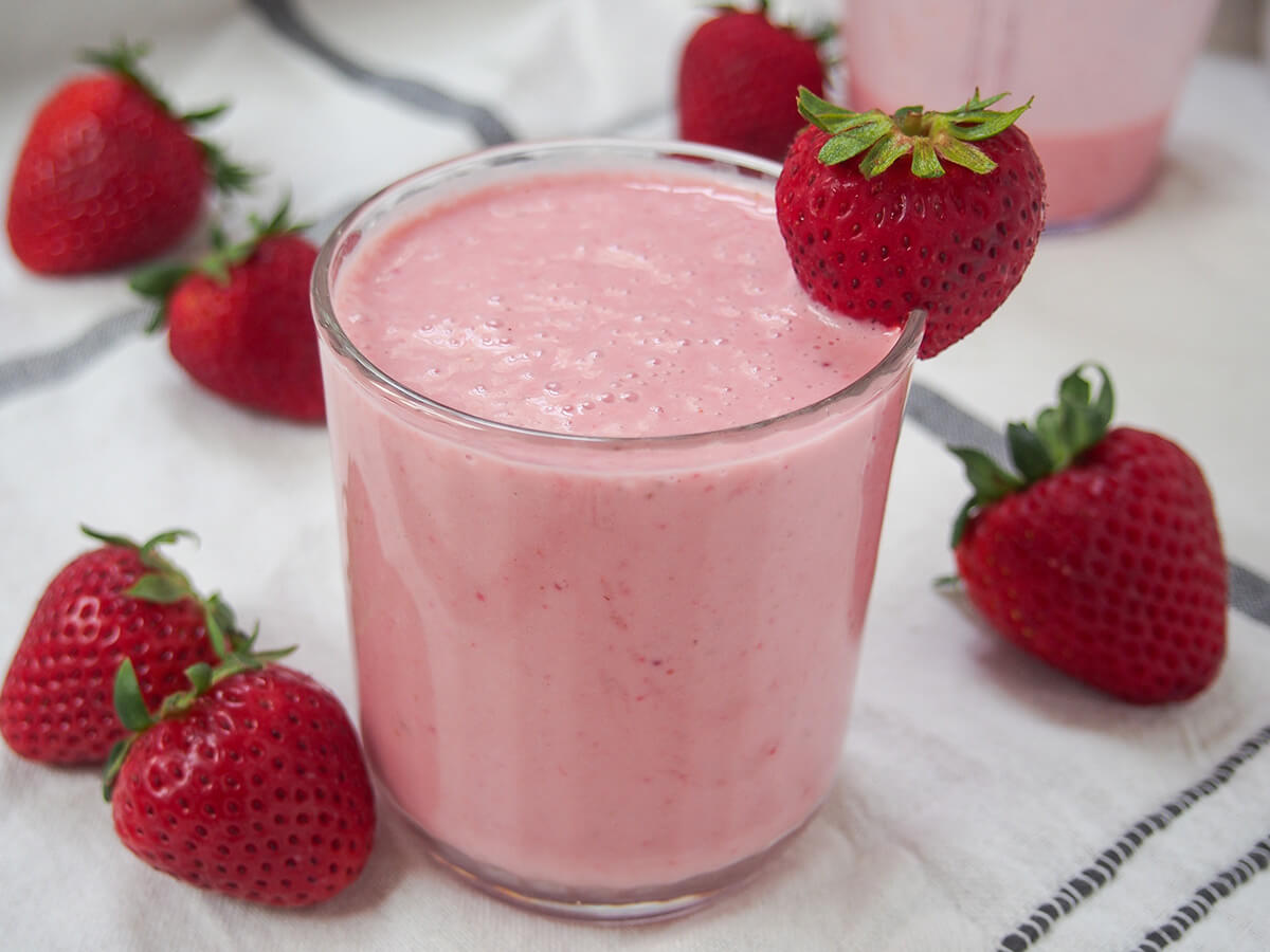 side view of a glass of strawberry lassi with strawberries either side.