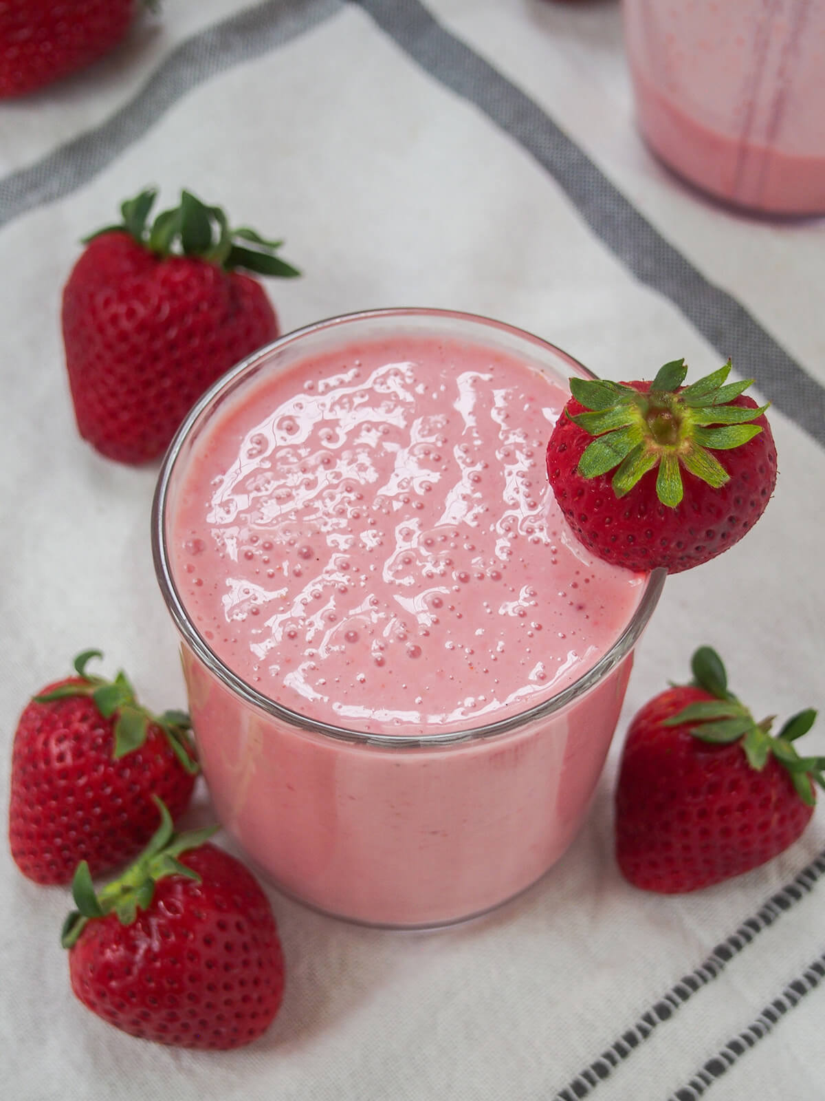 glass of strawberry lassi with strawberries around glass and bubbles on top of glass.