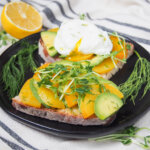two slices of avocado tartine with golden beet with lemon in background behind plate.