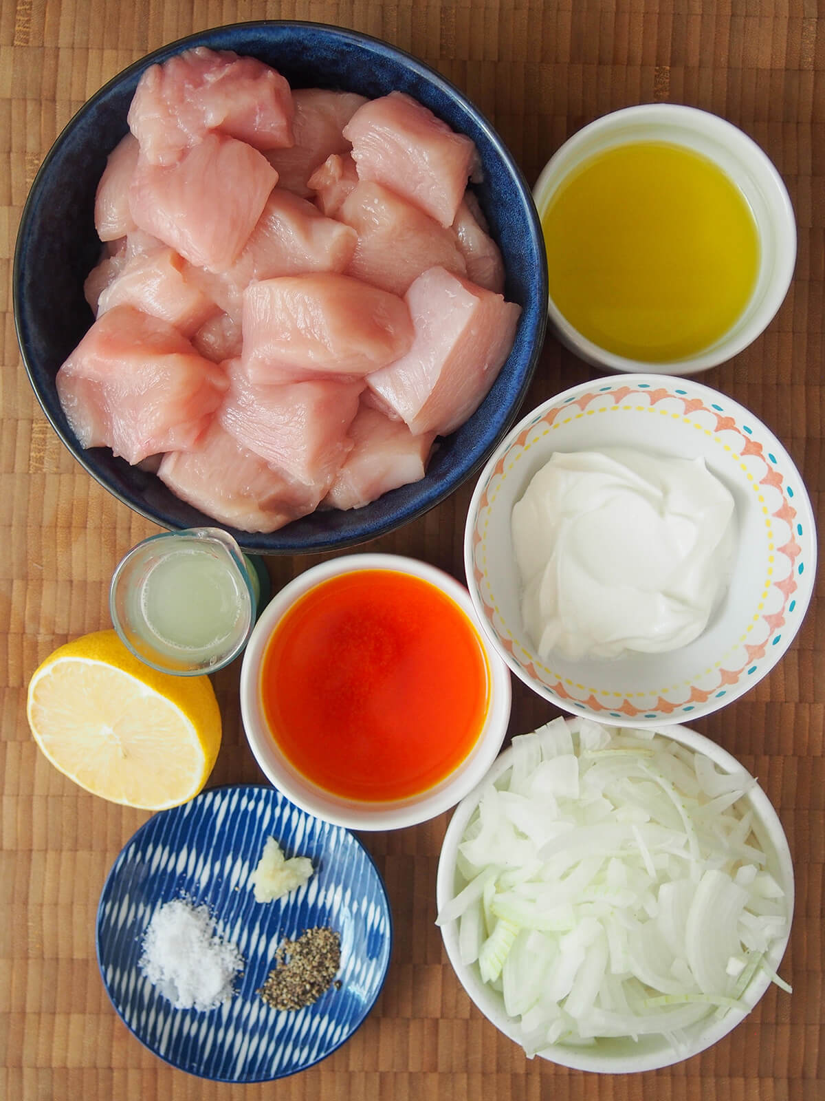 ingredients for joojeh kabab bowls with diced chicken, yogurt, sliced onion, olive oil, saffron water and lemon.