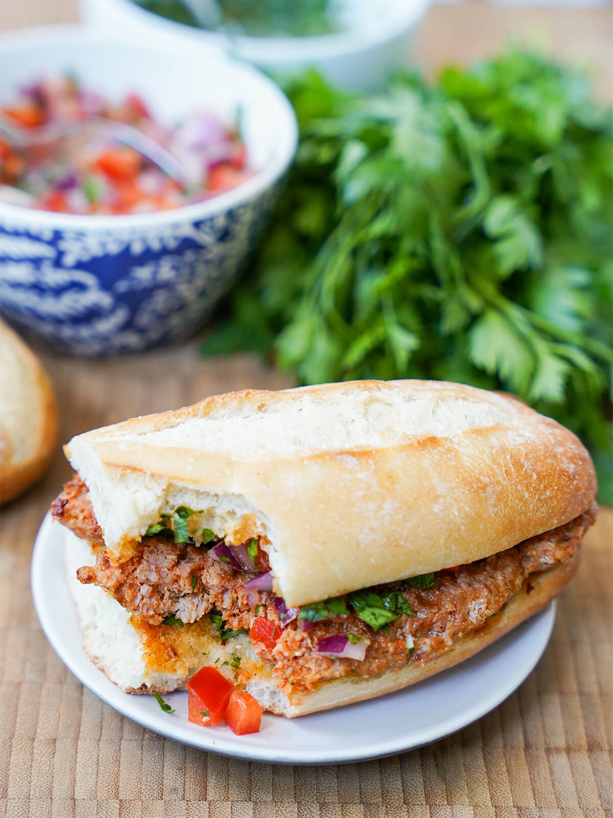 choripan Argentine chorizo sandwich with bite in corner sandwich with bite out of corner and some of salsa fallen onto plate and bowl with more behind.