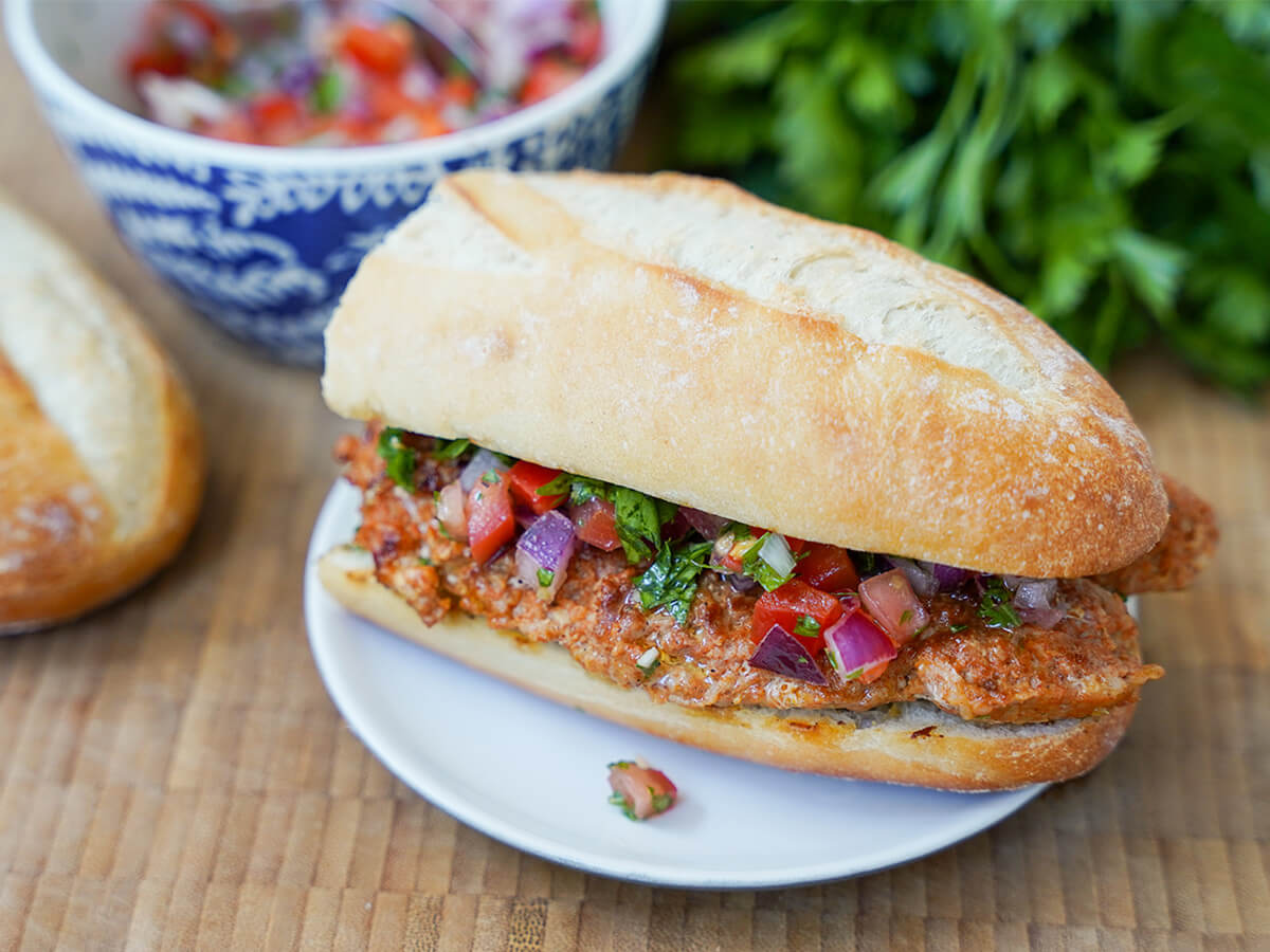 choripan Argentine chorizo sandwich on plate choripan, Argentine chorizo sandwich, on plate with bowl of salsa and parsley blurred in background behind.