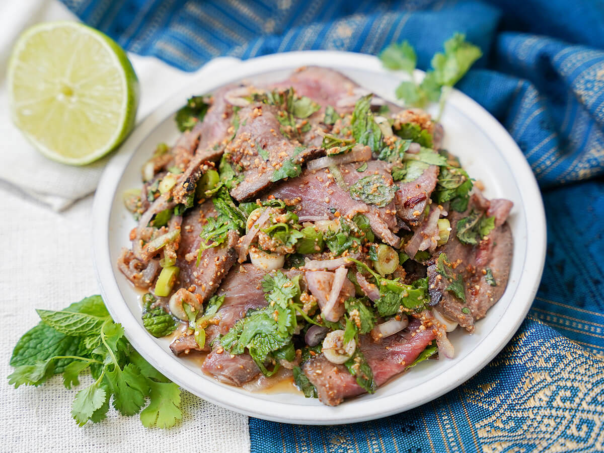 Thai beef salad (Nam Tok, 'waterfall beef') plate of nam tok waterfall beef with half lime and herbs to one side.