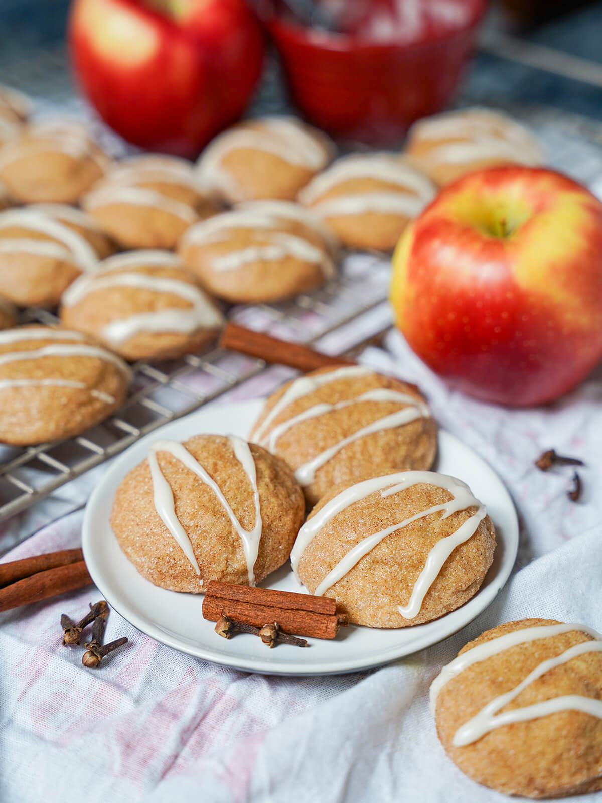 plate of apple cider cookies with cinnamon sticks, apple and more cookies to side of plate.