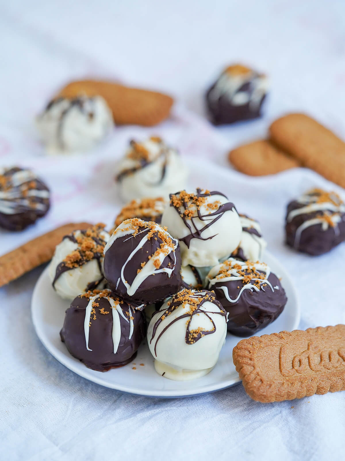 Biscoff truffles are really easy to make and a wonderfully indulgent, tasty and impressive-looking treat. Great for gifting, as a festive treat and really any excuse!  small plate of biscoff truffles with biscoff cookies and additional truffles to side and behind.