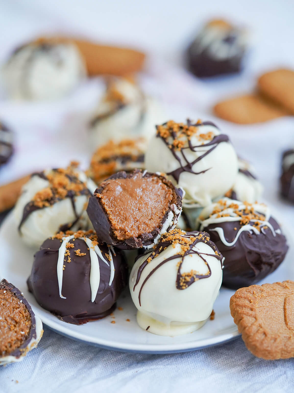 Biscoff truffles are really easy to make and a wonderfully indulgent, tasty and impressive-looking treat. Great for gifting, as a festive treat and really any excuse!  closer view of a cut biscoff truffle resting on top of stack of whole truffles.