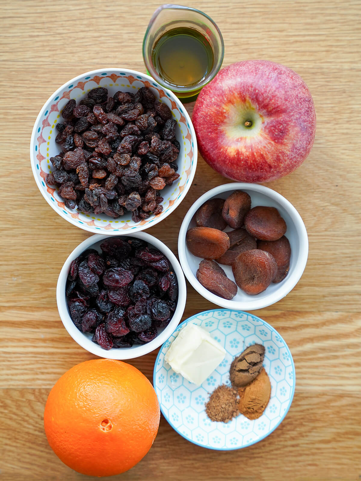 bowls of raisins, apricots, cranberries, spices with apple, orange and measure of brandy around.