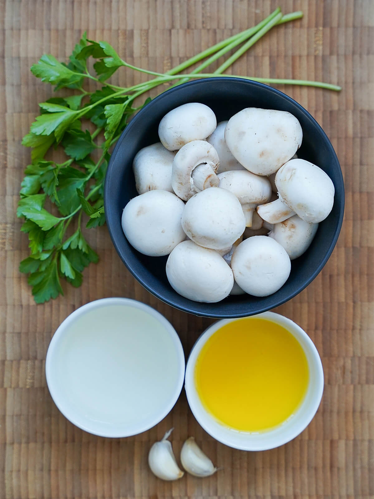 bowls of mushrooms, olive oil, wine with parsley and garlic cloves to side.