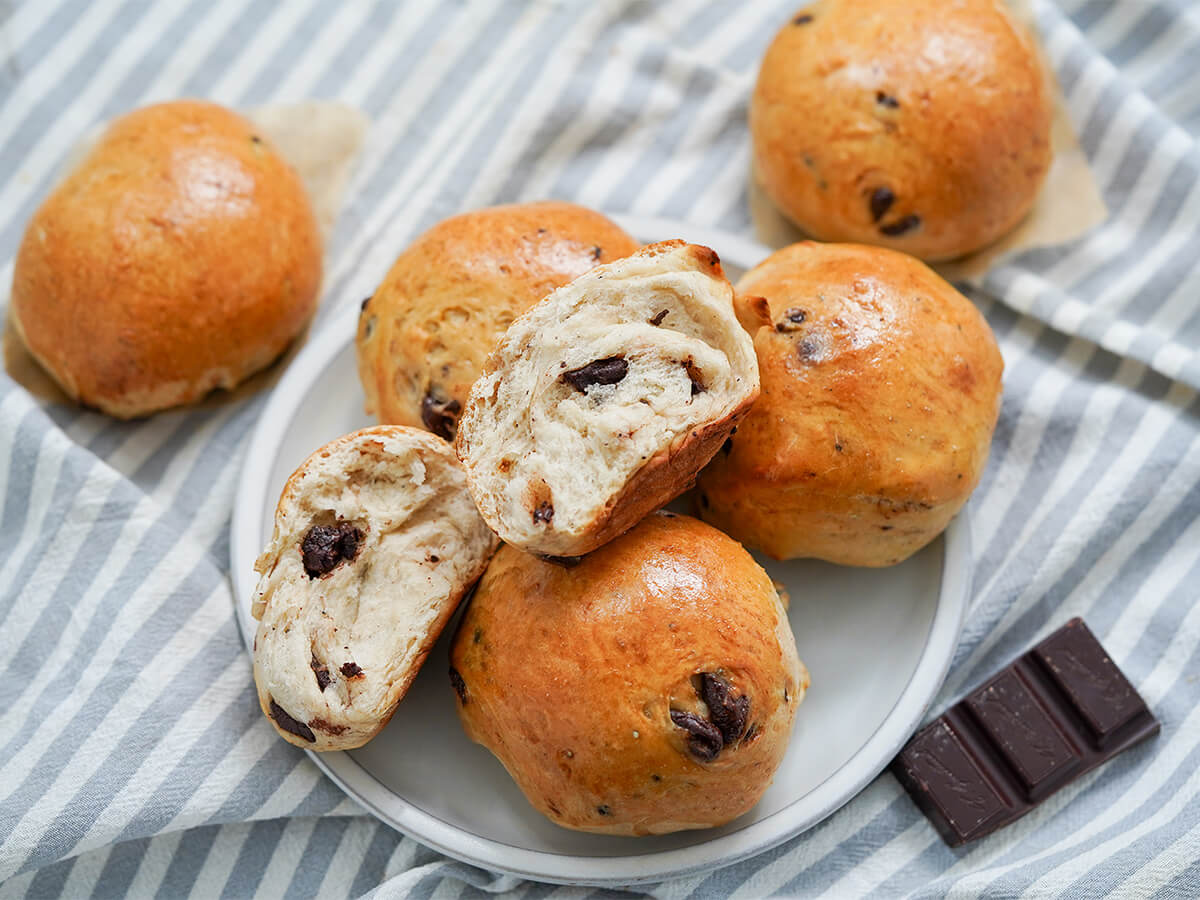 plate of Norwegian chocolate buns, sjokoladeboller, with one open showing chunks of chocolate inside and piece of chocolate to side.
