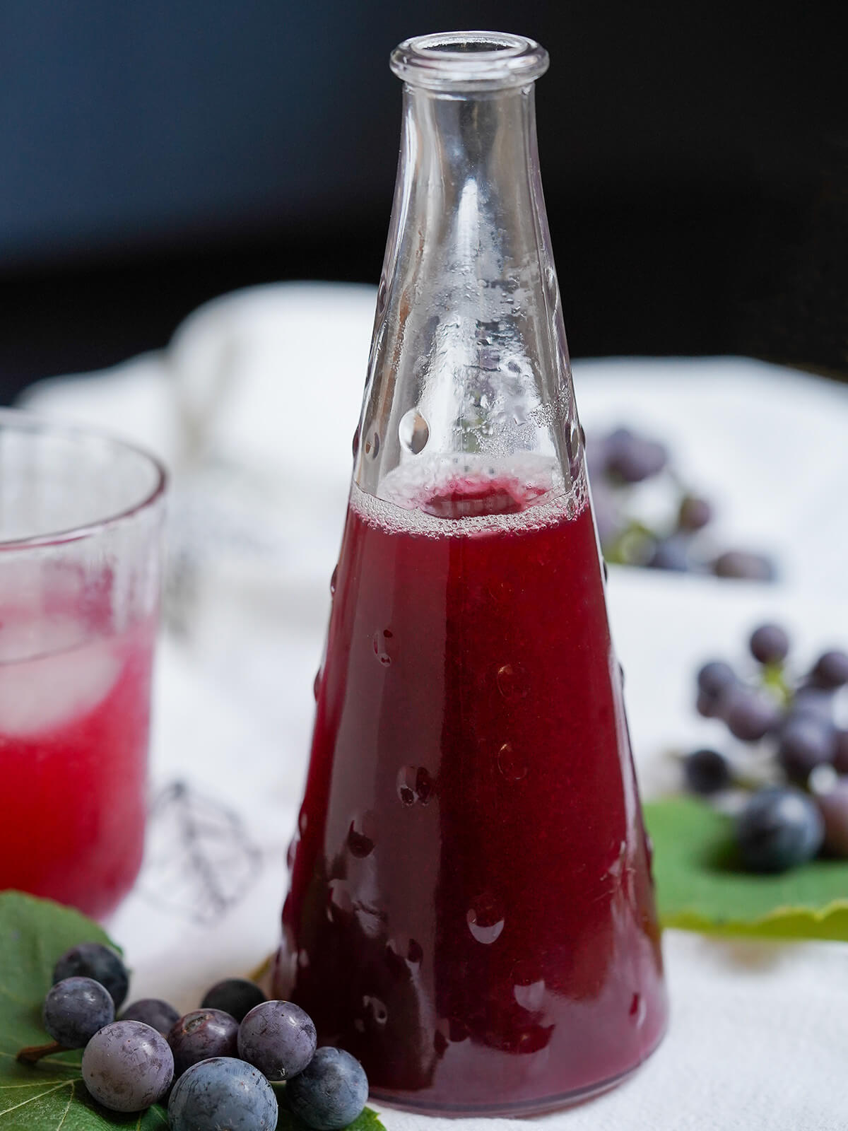 bottle of concord grape syrup with grapes blurred behind.