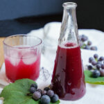 bottle of grape syrup with glass made into soda to side and grapes in between.
