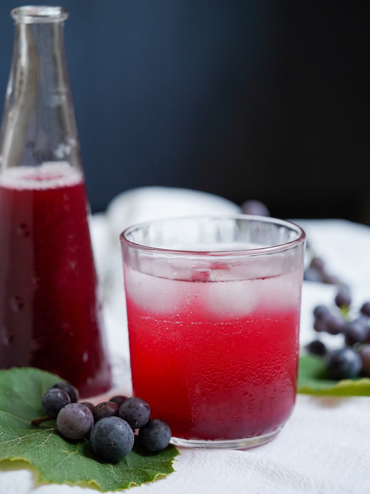 glass of grape soda with bottle of syrup behind.