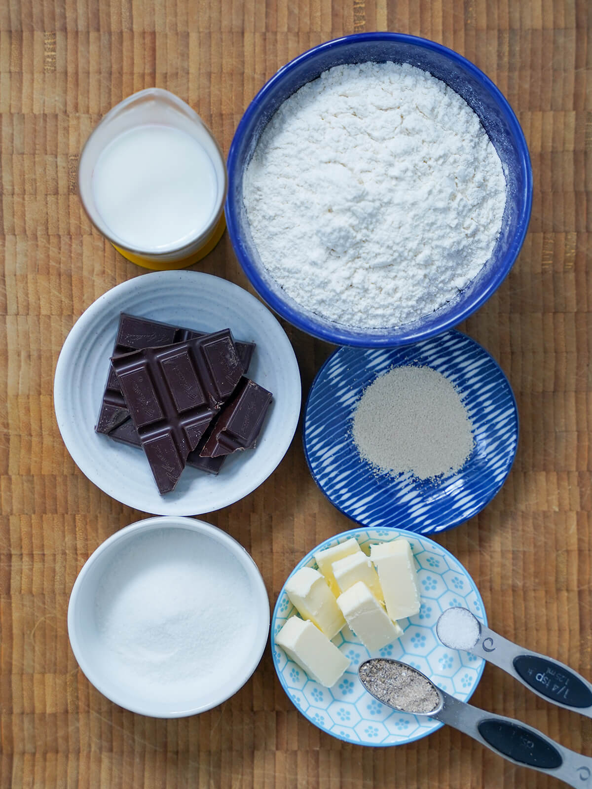 bowls with flour, yeast, chocolate, sugar, butter and a measure of milk, spoons with cardamom and salt.