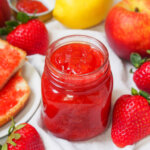 jar of strawberry peach jam with fruit all around it.