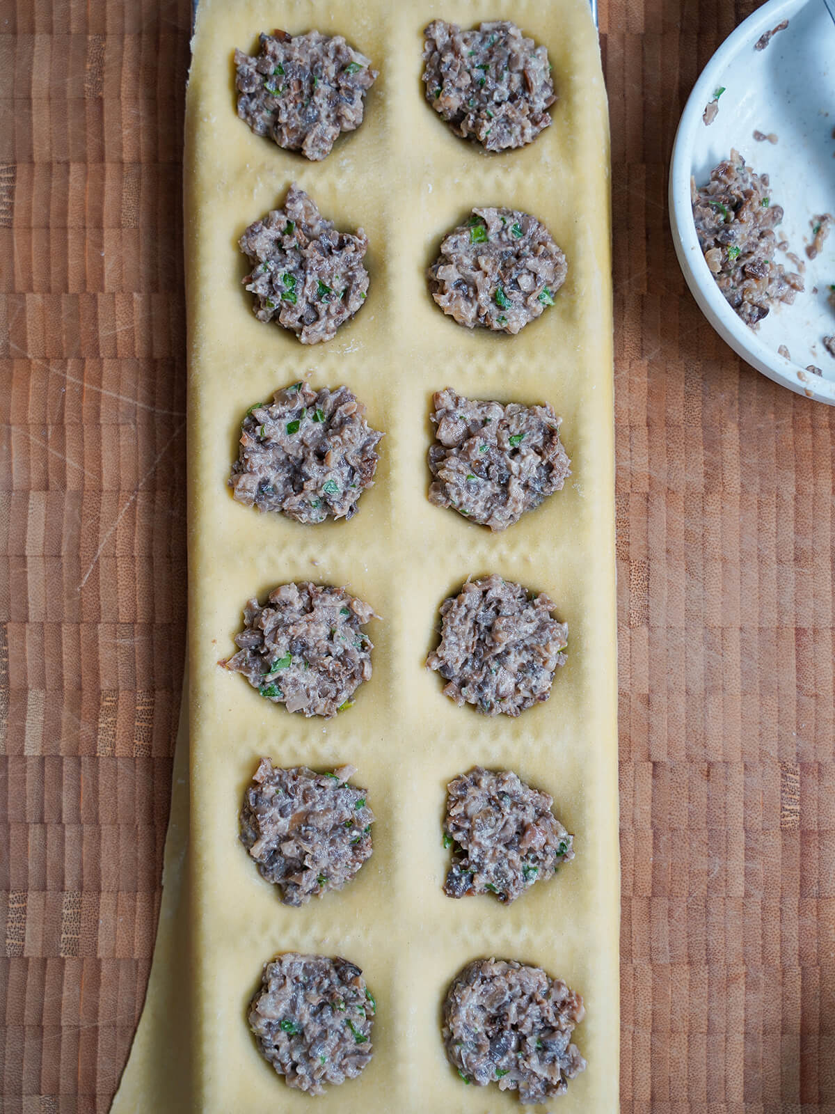 mushroom filling in indents in piece of pasta in ravioli mould mushroom filling on top of pasta dough in mould.