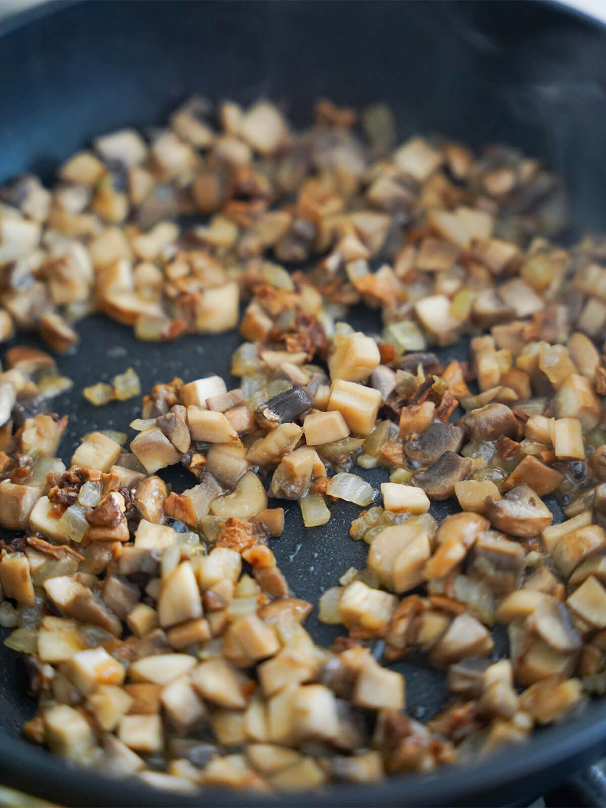 cooking mushrooms in skillet for mushroom ravioli diced mushroom and porcini cooking in skillet with fine diced onion.