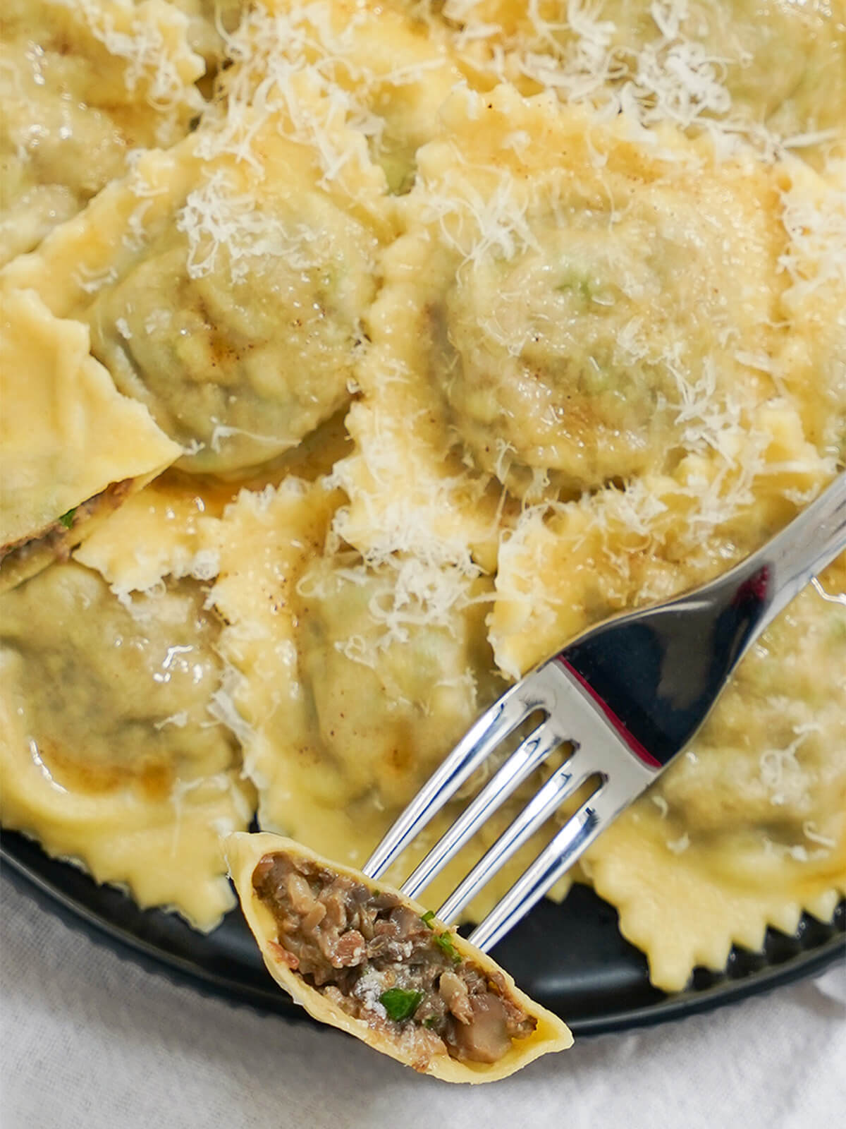 These mushroom ravioli have a delicious earthy, creamy filling that's both comforting and relatively light. Both fresh mushrooms & dried porcini help make these a really flavorful homemade pasta. close view of cut open mushroom ravioli on fork over plate with more ravioli.