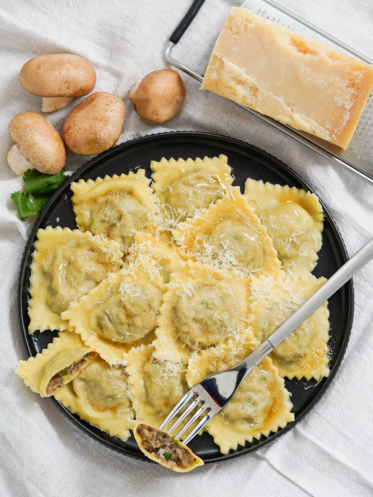 These mushroom ravioli have a delicious earthy, creamy filling that's both comforting and relatively light. Both fresh mushrooms & dried porcini help make these a really flavorful homemade pasta. plate of mushroom ravioli with block of parmesan and some mushrooms above plate.