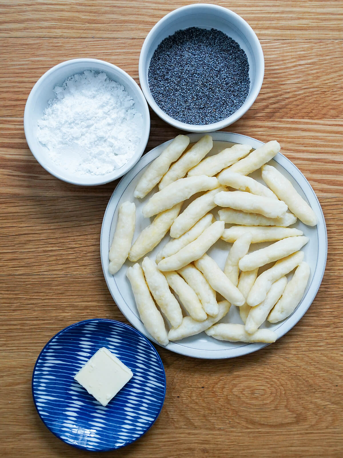 plate of part cooked schuplnudeln, dishes with butter, poppy seeds and powdered sugar.