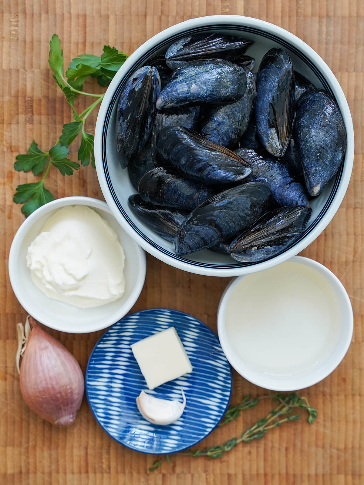 bowls of mussels, cream, wine, butter, garlic with shallot, sprigs of thyme and parsely around.