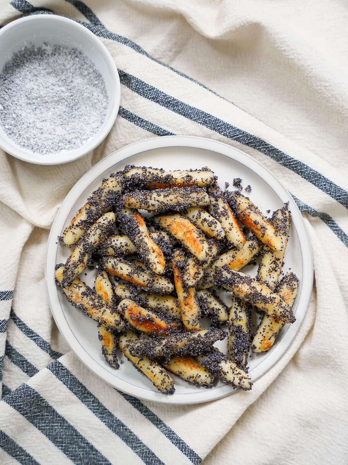 overhead view of plate of mohnnudeln, poppy seed potato noodles with dish of poppy seed and sugar mixture above.