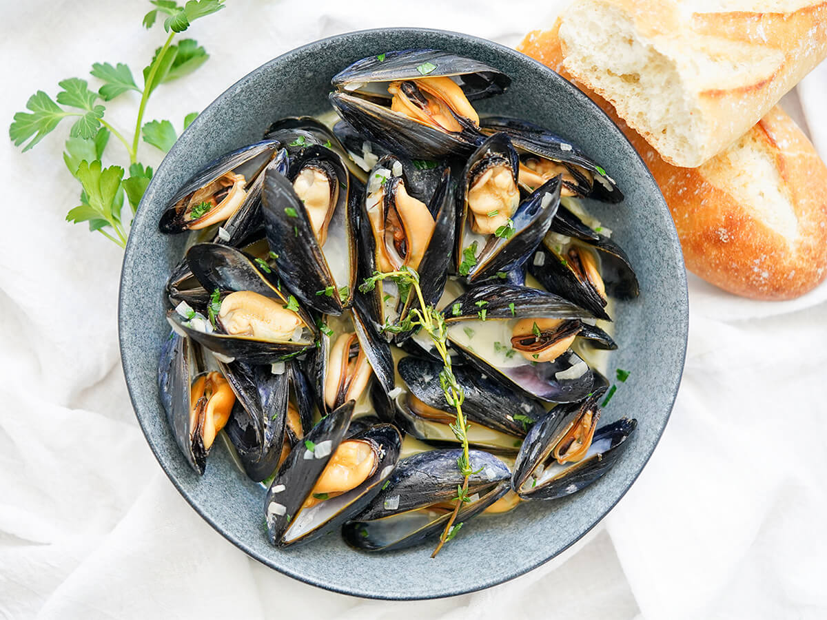 bowl of mussels in cream with chunks of baguette above bowl.