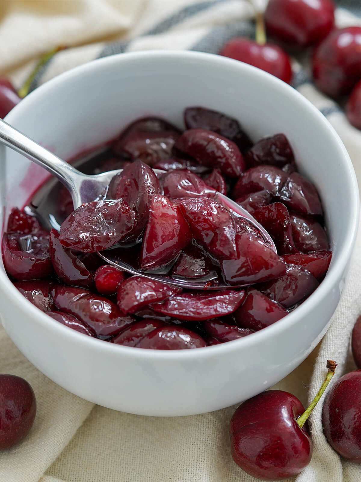 spoon of cherry compote sitting in bowl with more.