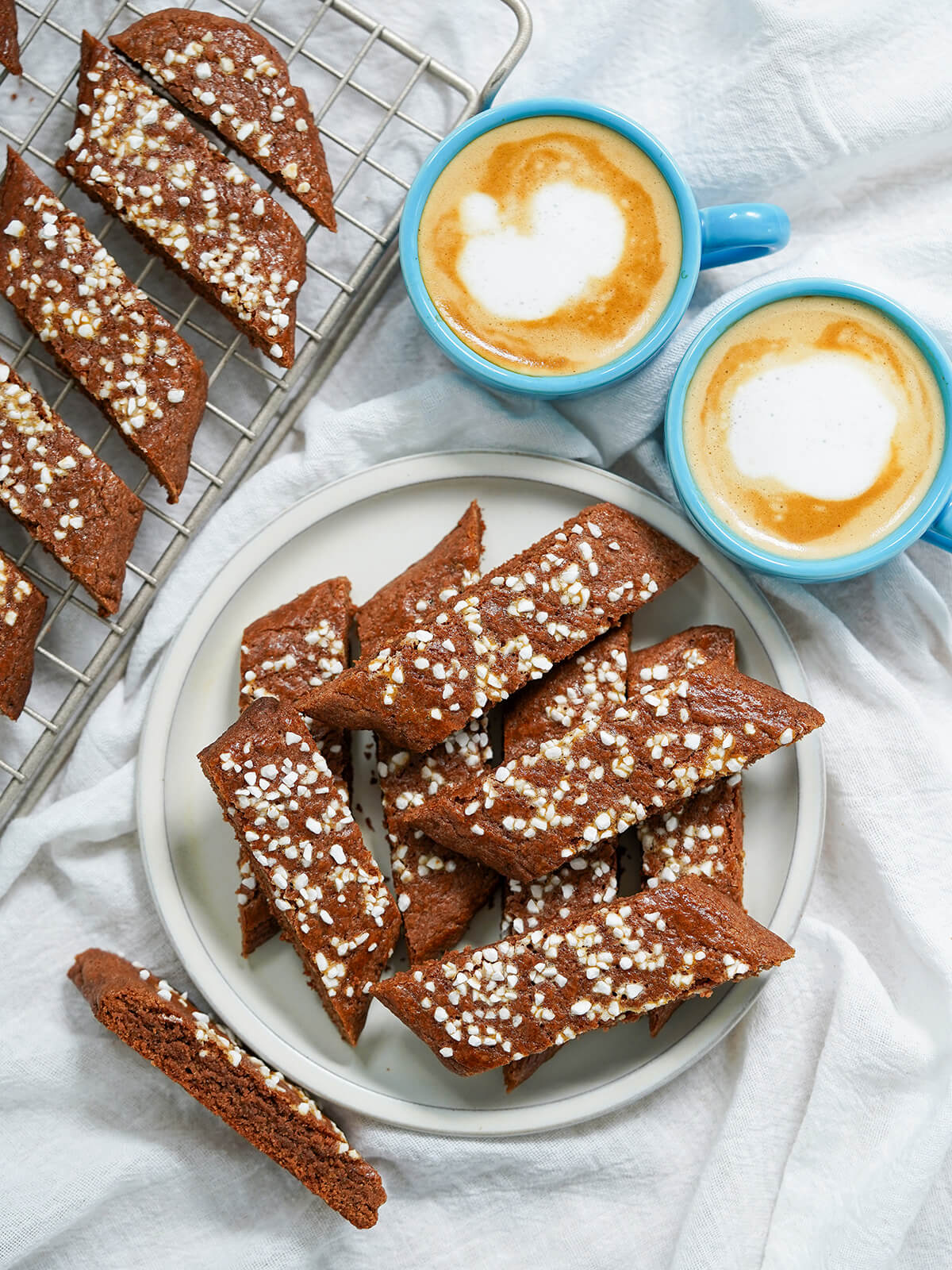 overhead view of plate of chokladsnittar. Swedish chocolate cookies with cups of coffee above plate and more cookies on cooling rack to side.
