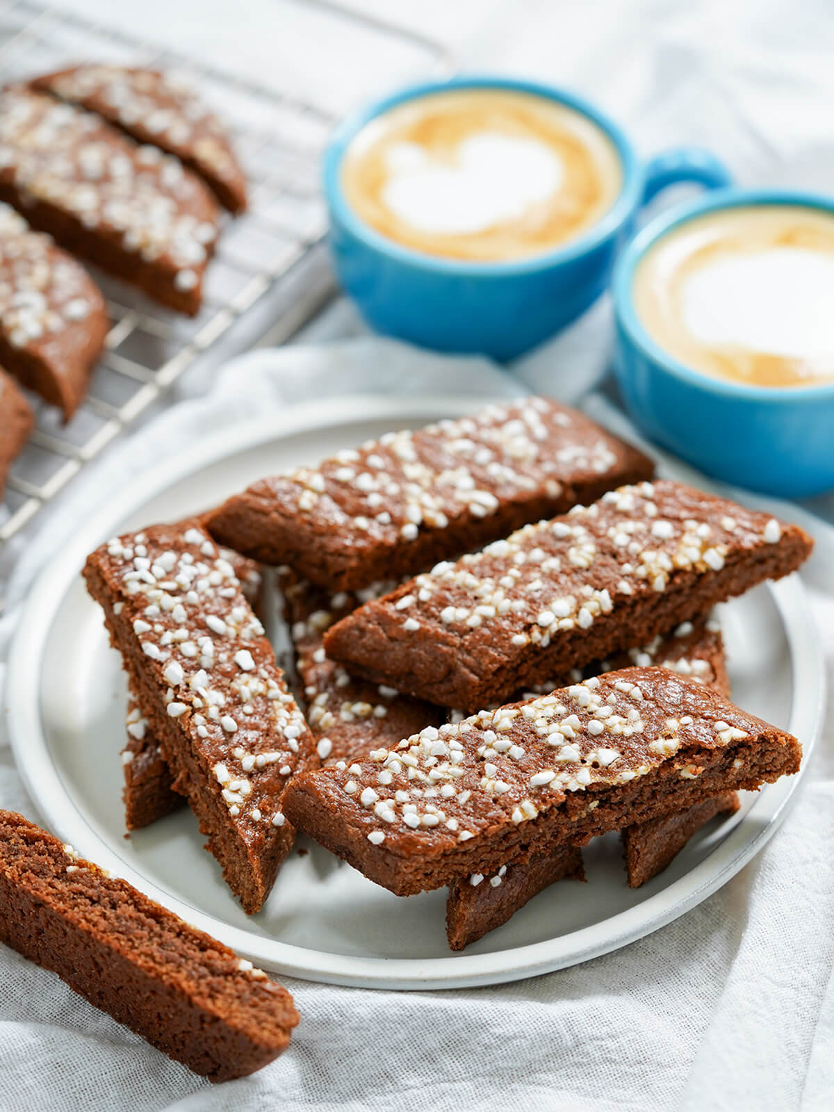 chokladsnittar, Swedish chocolate cookies on a plate with cups of coffee in background.