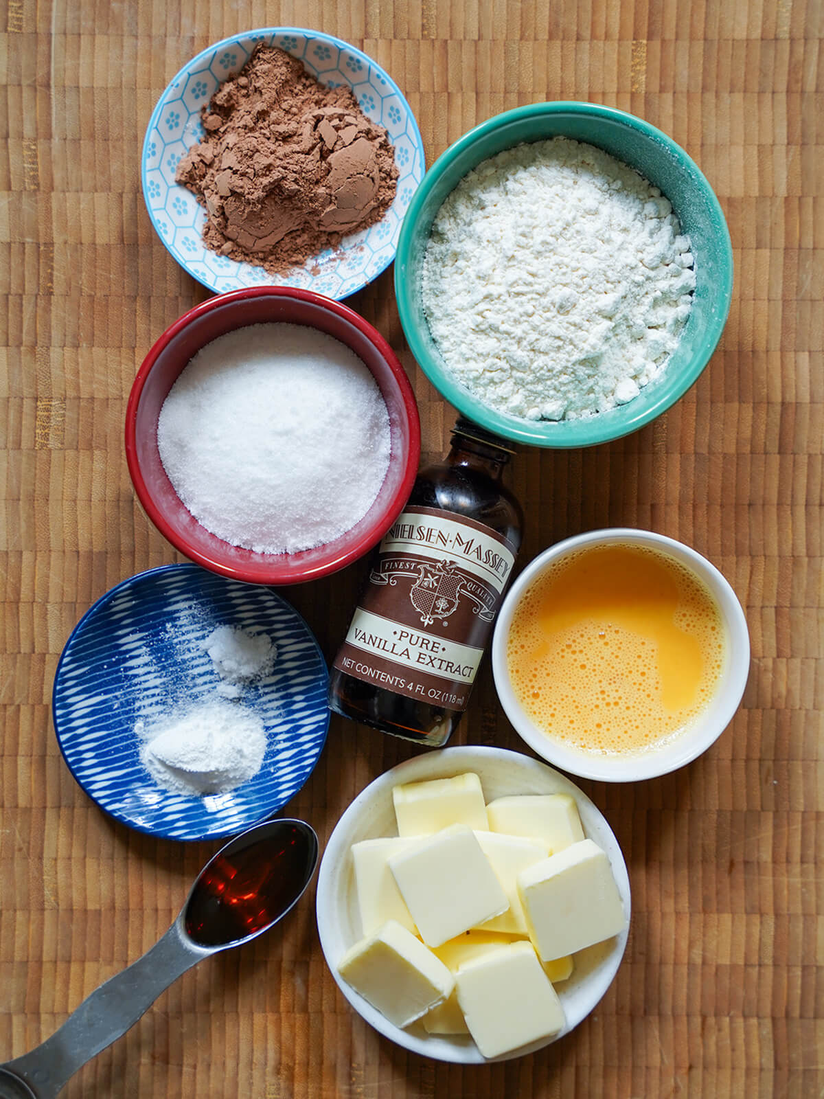 ingredients for chokladsnittar, Swedish chocolate cookie slices bowls of flour, cocoa powder, sugar, egg, butter with vanilla bottle in middle and spoon of golden syrup to side.