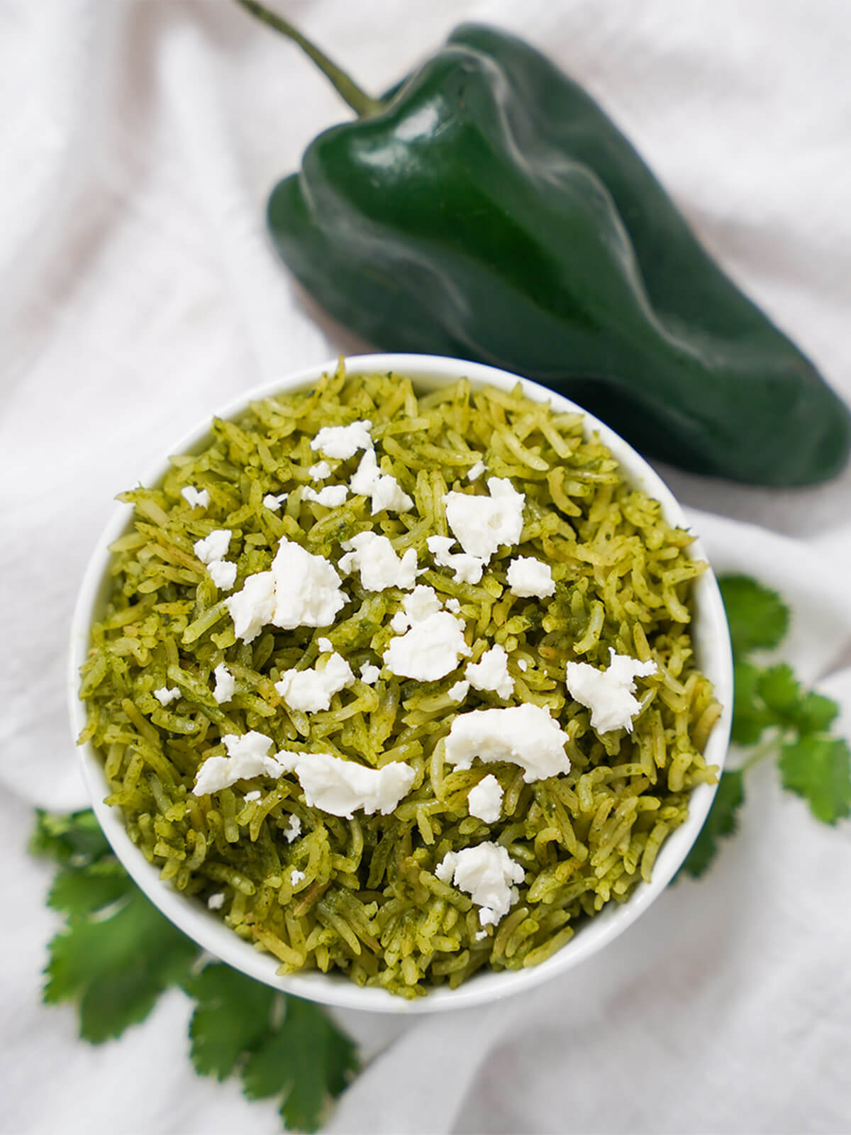 Mexican green rice, arroz verde, is an easy and delicious way to add fantastic flavor and color to make your side shine. Great in burritos, alongside enchiladas and more. bowl of arroz verde Mexican green rice with poblano pepper above bowl.