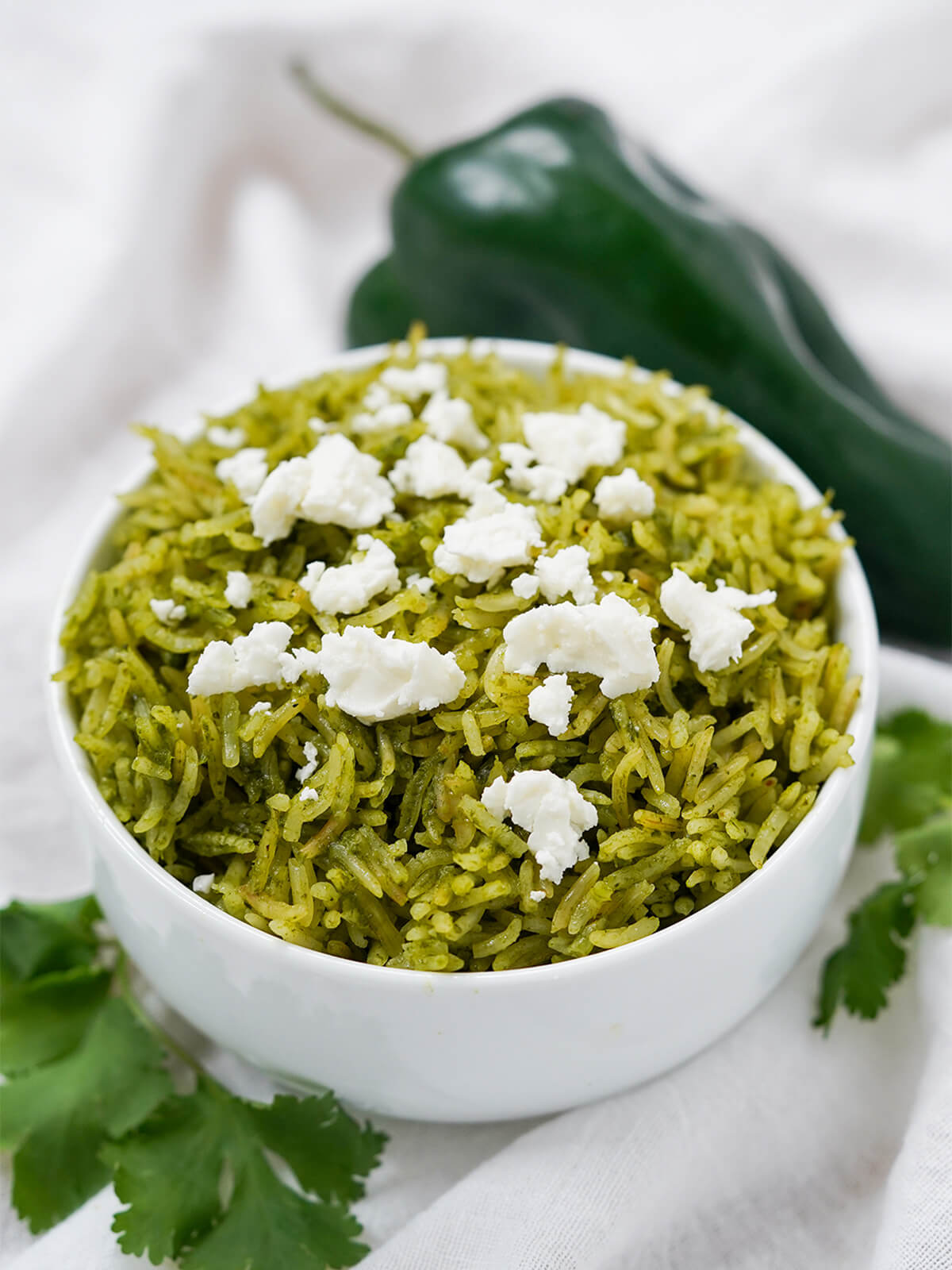 Mexican green rice, arroz verde, is an easy and delicious way to add fantastic flavor and color to make your side shine. Great in burritos, alongside enchiladas and more. bowl of arroz verde Mexican green rice with poblano behind and cilantro in front of bowl.