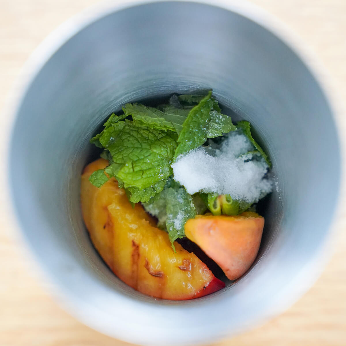 slices of peach, mint leaves and sugar in cocktail shaker.