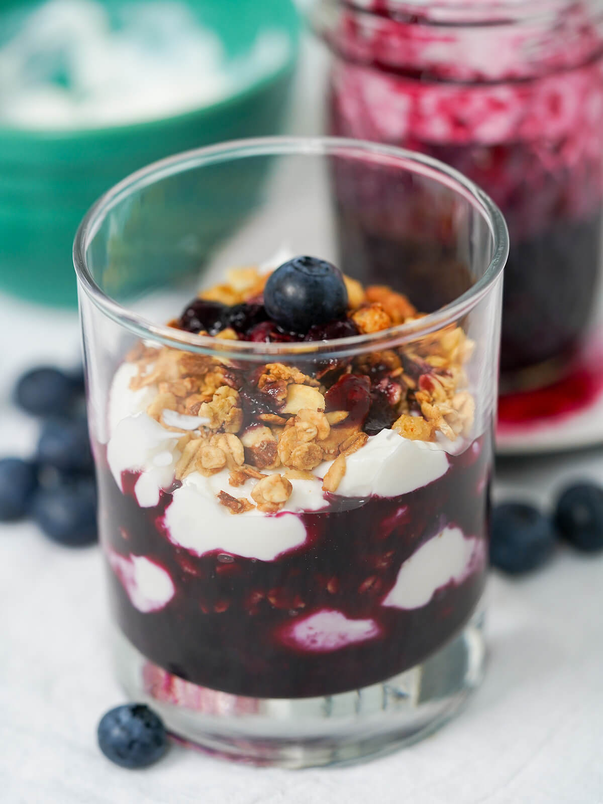 side view of glass of blueberry parfait showing yogurt and blueberry layers and granola part mixed in.