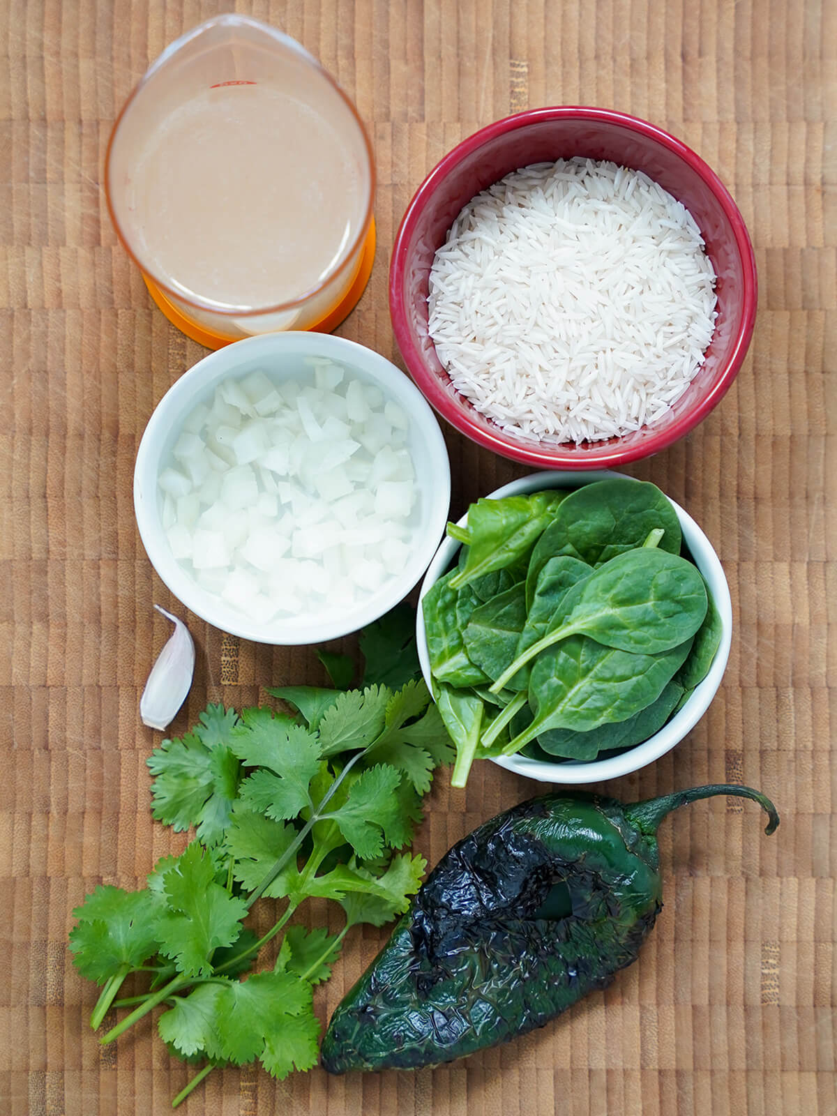 ingredients for arro verde, Mexican green rice bowls of rice, onion, spinach with measure of stock, bunch of cilantro and charred poblano to side.